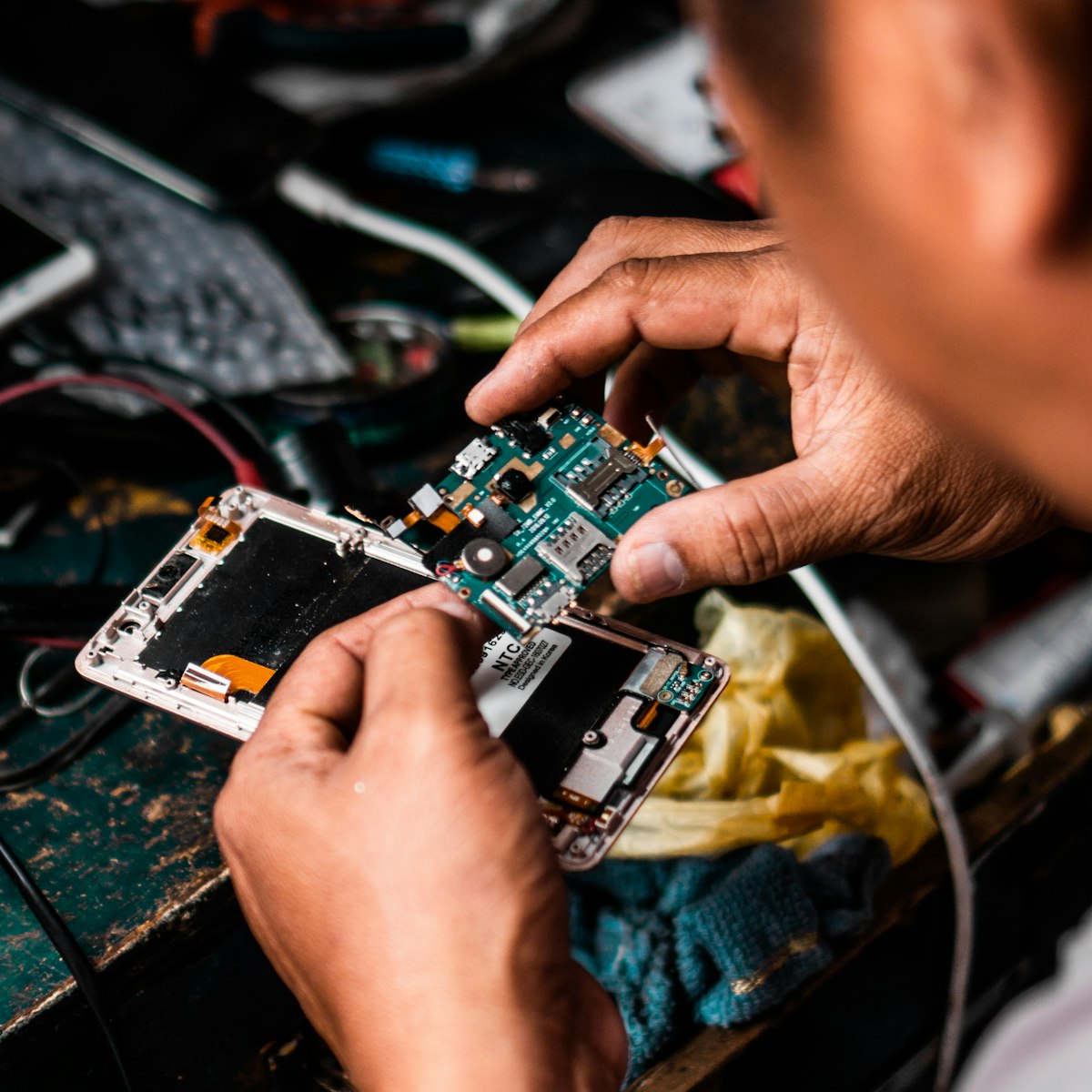 A technician's hands repairing the internal circuit board of a smartphone.